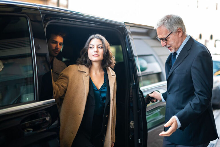 Woman exiting luxury car, guided by chauffeur.